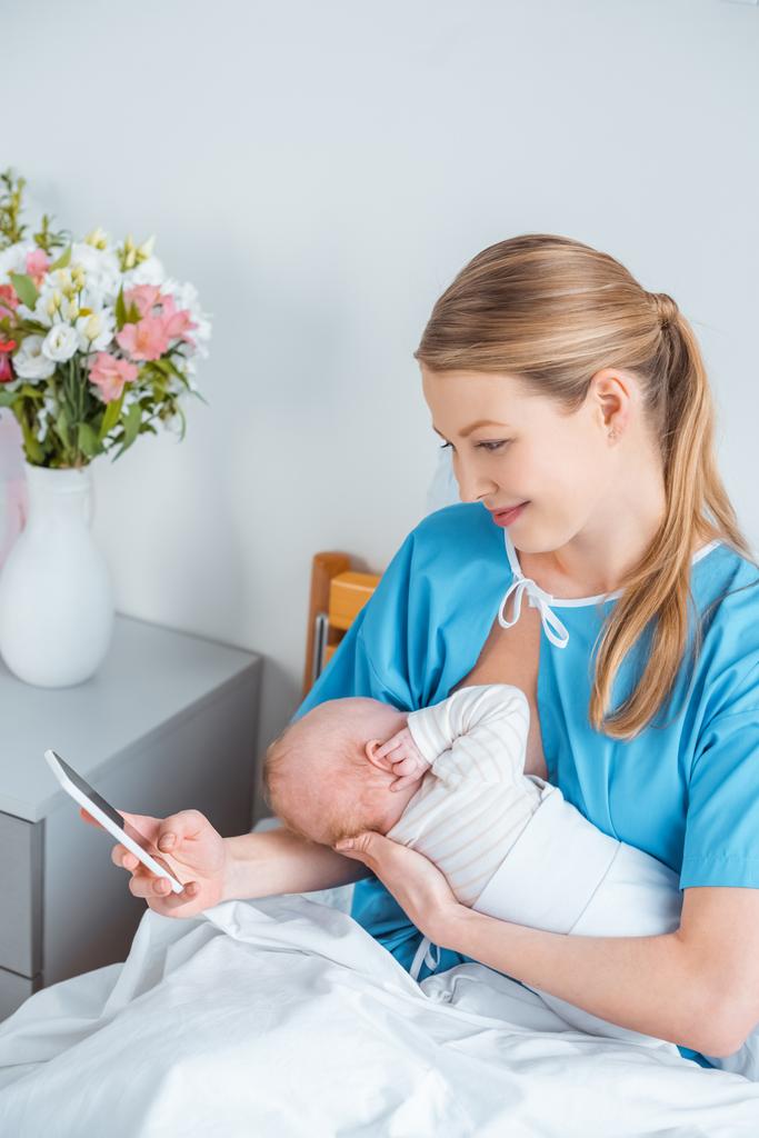 visão de alto ângulo de sorrir jovem mãe amamentando bebê e usando smartphone no quarto do hospital
 - Foto, Imagem