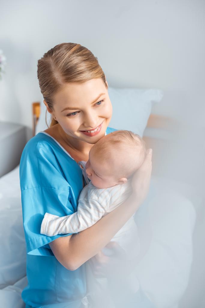 високий кут зору усміхненої молодої матері тримає чарівну дитину в лікарняній кімнаті
 - Фото, зображення