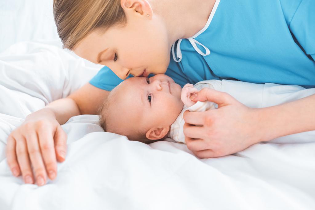 Yeni doğan bebek yatak hastane odasında yatan öpüşme genç anne - Fotoğraf, Görsel