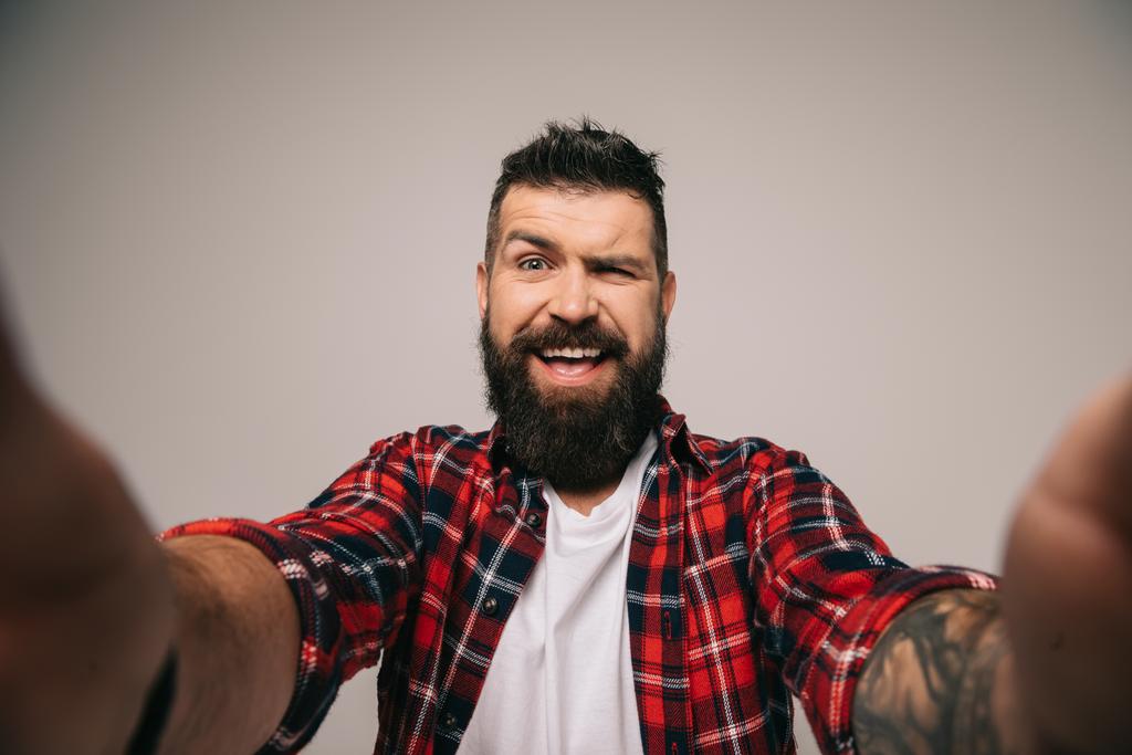 göz kırpıyor ve selfie, gri izole alarak neşeli sakallı adam - Fotoğraf, Görsel