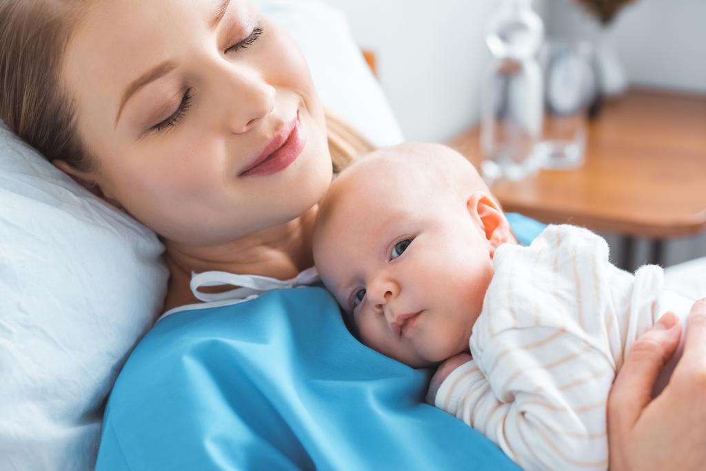 Szczęśliwa młoda matka z zamkniętymi oczami leżącego z noworodek noworodka na piersi w szpitalu - Zdjęcie, obraz