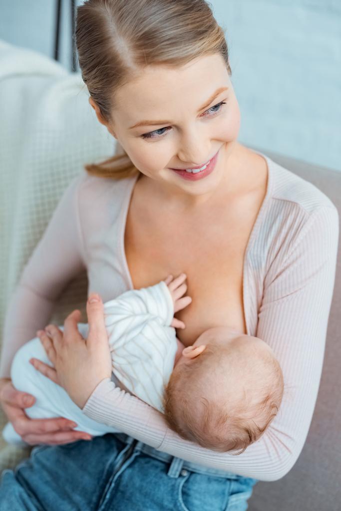 счастливая молодая женщина кормит грудью младенца дочь и глядя в сторону дома
 - Фото, изображение