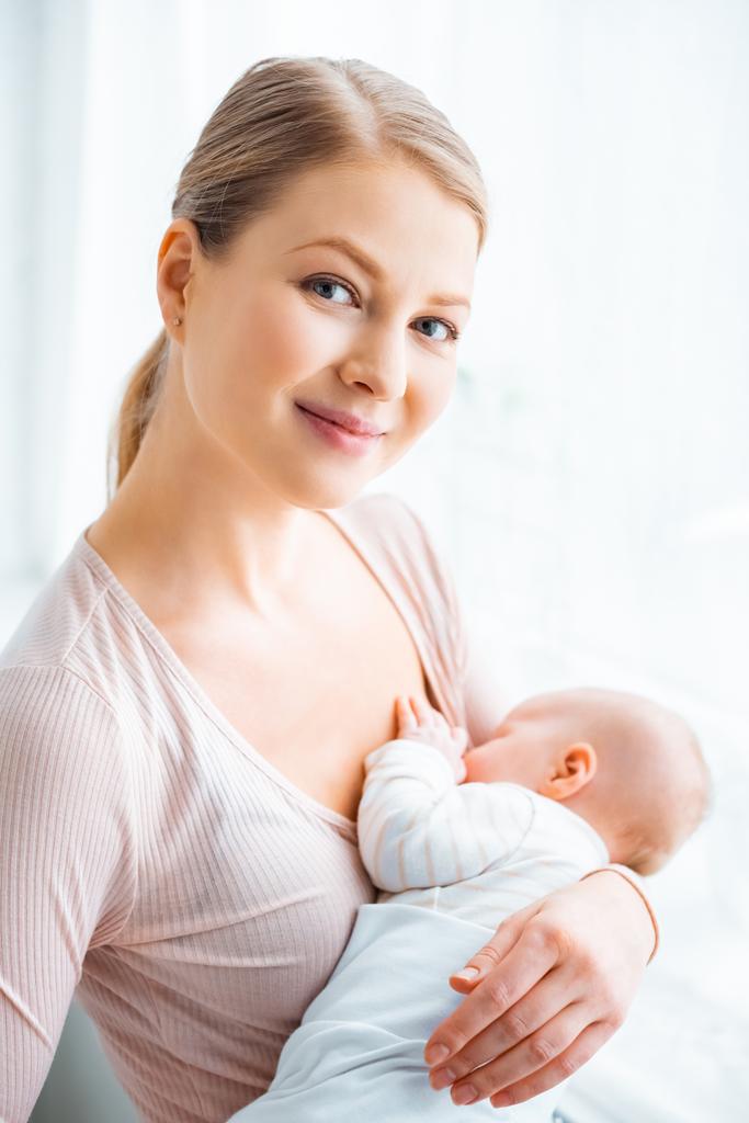 beautiful young mother breastfeeding baby and smiling at camera - Photo, Image
