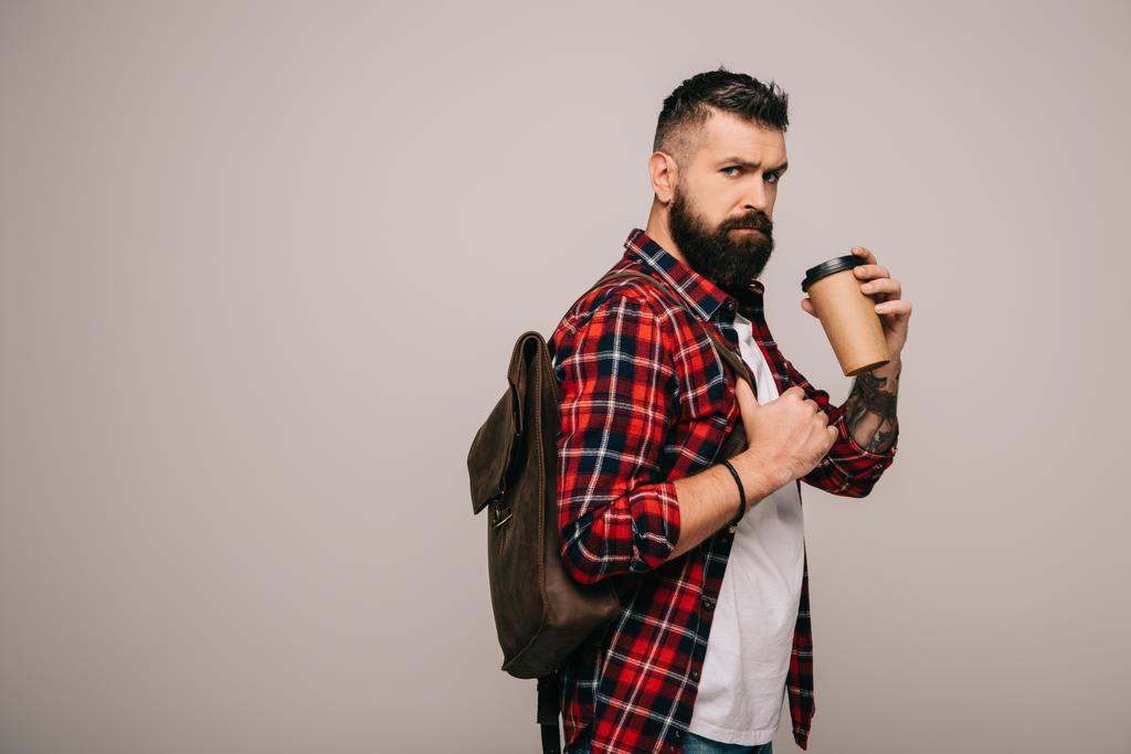 serious bearded man in checkered shirt with backpack holding coffee to go isolated on grey - Photo, Image