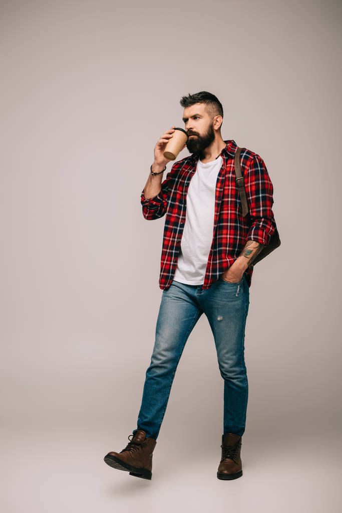 vousatý muže v kostkované košili chůzi a pití kávy, aby izolované na šedá - Fotografie, Obrázek
