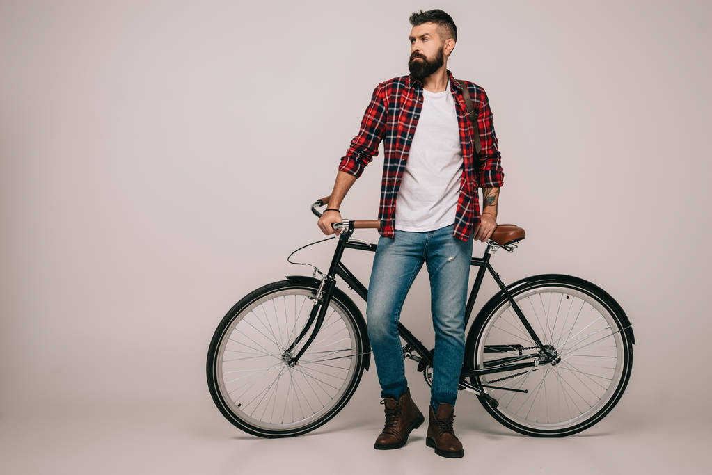Bärtiger Mann im karierten Hemd steht am Fahrrad auf grau - Foto, Bild