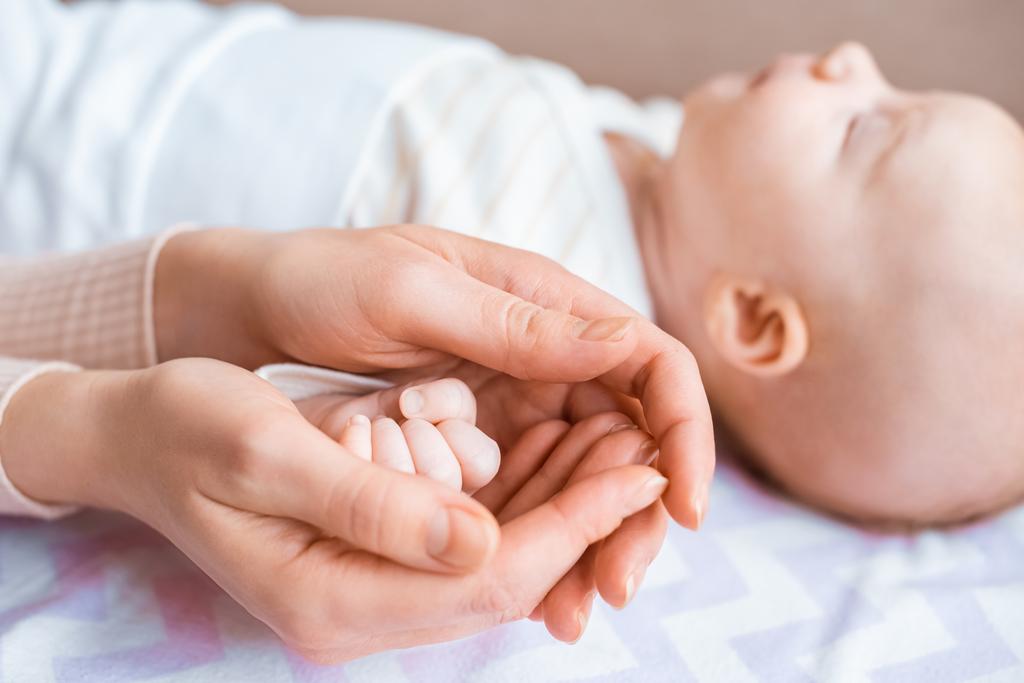 Schnappschuss von Mutter, die Hand auf entzückendem Säugling hält, der auf Sofa liegt - Foto, Bild