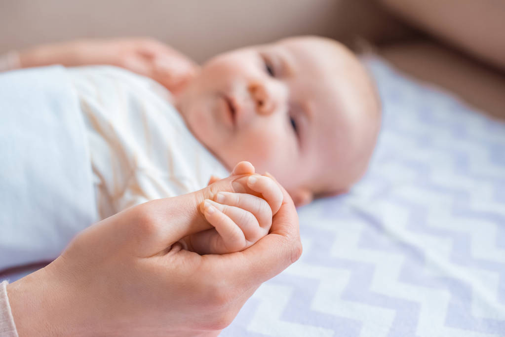 Schnappschuss von Mutter, die Hand auf entzückendem Säugling hält, der auf Couch liegt - Foto, Bild