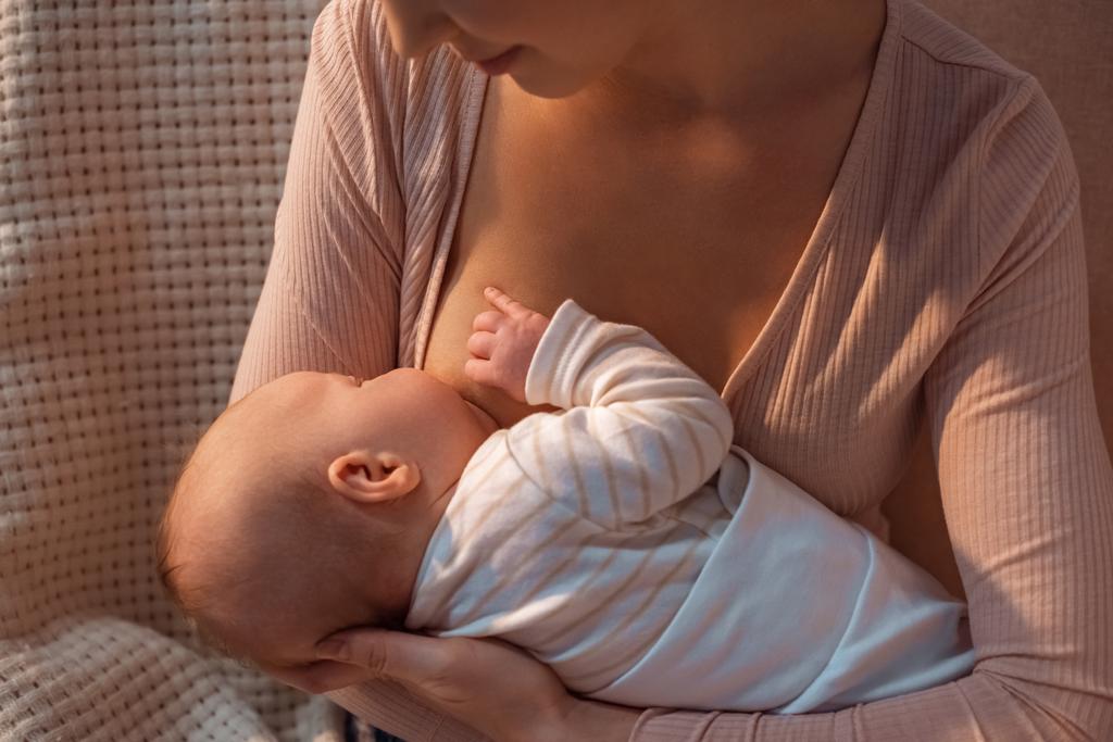 bijgesneden schot van jonge moeder borstvoeding baby's nachts - Foto, afbeelding