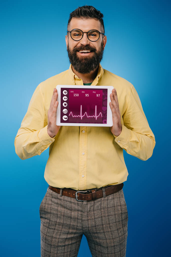 uśmiechający się Brodaty mężczyzna wyświetlone cyfrowego tabletu z danych o stanie zdrowia, na niebieskim tle - Zdjęcie, obraz