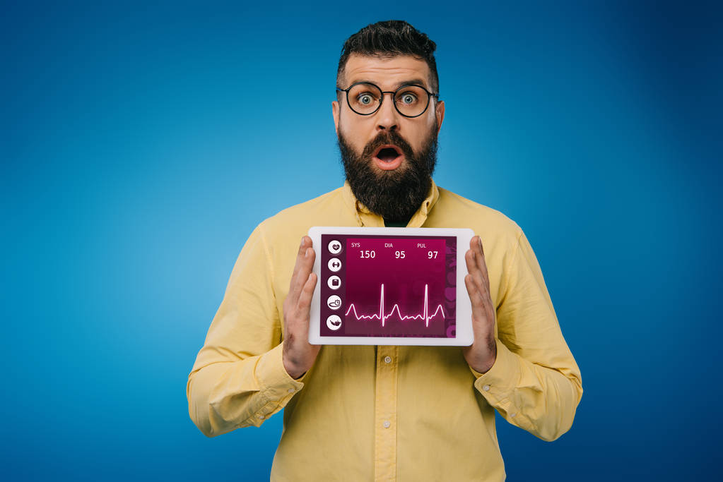 Šokovaný vousatý muž představují digitální tabletu s zdravotní údaje, izolované na modré - Fotografie, Obrázek