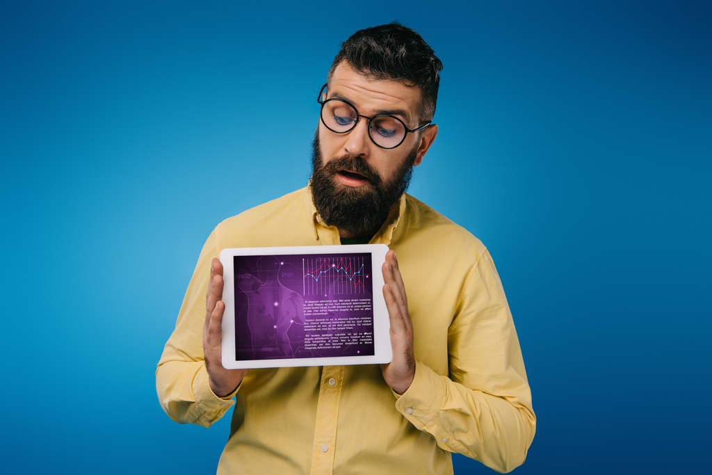 заинтересованный бородатый мужчина смотрит на цифровой планшет с инфографикой, изолированный на синий
 - Фото, изображение