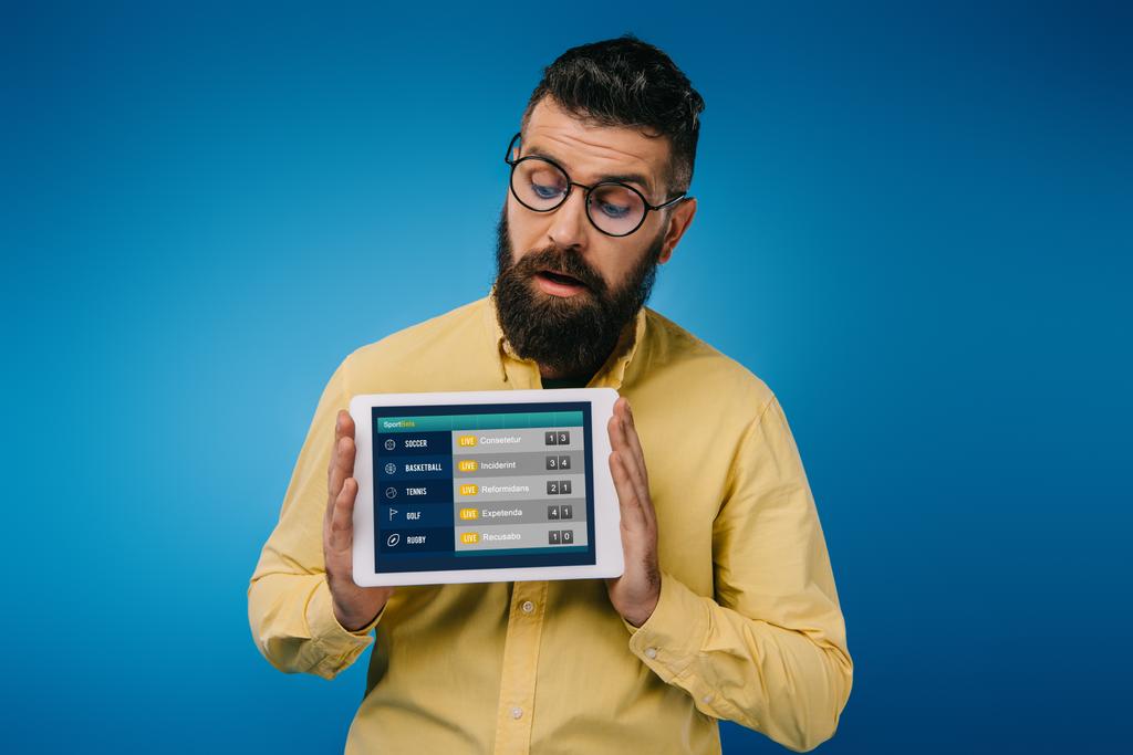 interessato uomo barbuto guardando tablet digitale con app sport, isolato su blu
 - Foto, immagini