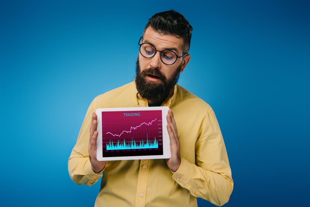 hombre barbudo interesado mirando tableta digital con aplicación tariding, aislado en azul
 - Foto, Imagen
