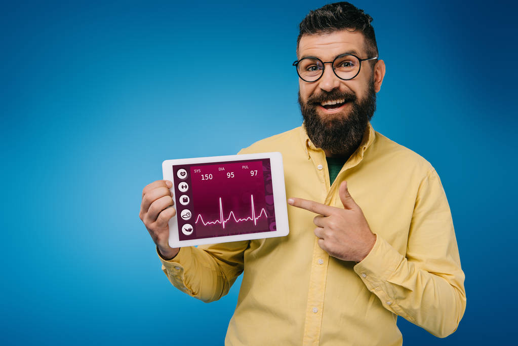 happy bearded man pointing at digital tablet with health data, isolated on blue - Photo, Image