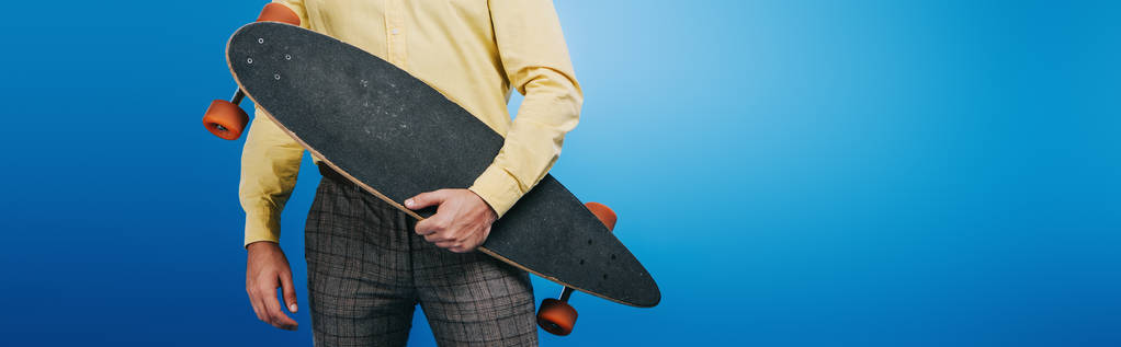 vista recortada del hombre sosteniendo longboard aislado en azul
 - Foto, Imagen