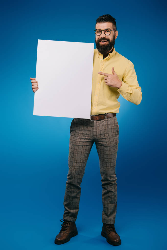 barbudo sonriente apuntando a un cartel vacío aislado en azul
 - Foto, Imagen