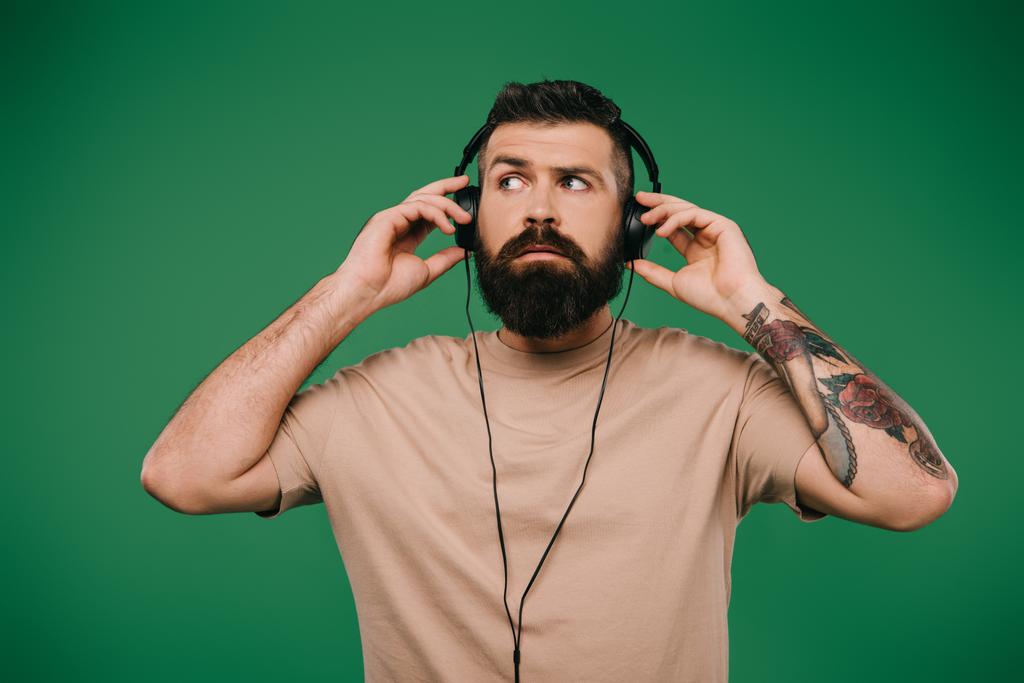 όμορφος άνδρας τατουάζ ακούγοντας μουσική στα ακουστικά που απομονώνονται σε πράσινο - Φωτογραφία, εικόνα