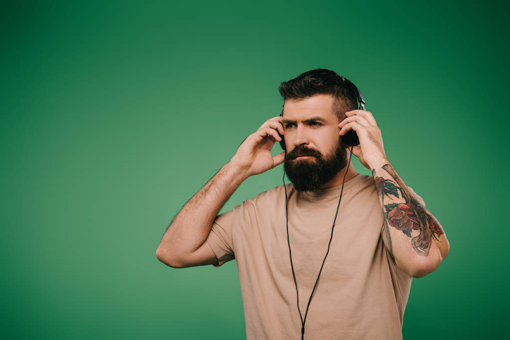 bearded tattooed man listening music in headphones isolated on green - Photo, Image