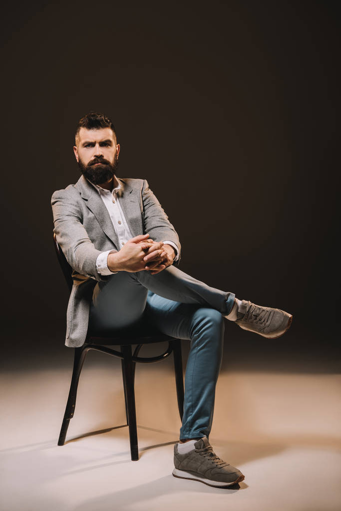 bel homme d'affaires barbe en veste grise assis sur une chaise isolée sur brun
 - Photo, image