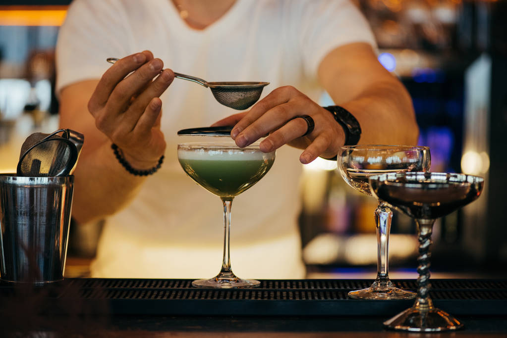 selectieve aandacht van barman voorbereiden alcoholische cocktail met behulp van sieve - Foto, afbeelding