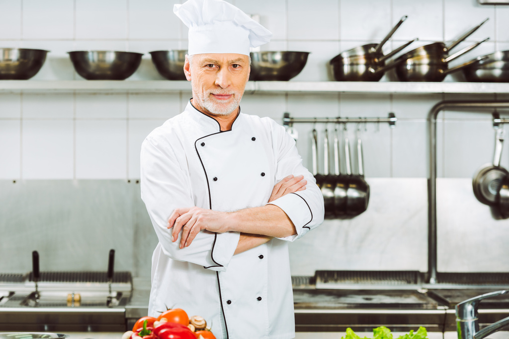 guapo chef masculino en uniforme con los brazos cruzados mirando a la cámara en la cocina del restaurante
 - Foto, imagen