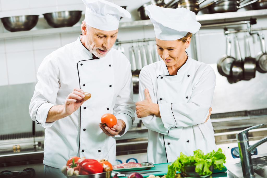 női és férfi szakácsok kétsoros gombolású kabátok és sapkák étterem konyha főzés közben beszél - Fotó, kép