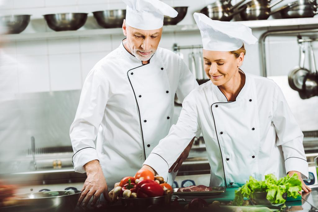 enfoque selectivo de chefs femeninos y masculinos en uniforme y sombreros de cocina en la cocina del restaurante
 - Foto, imagen