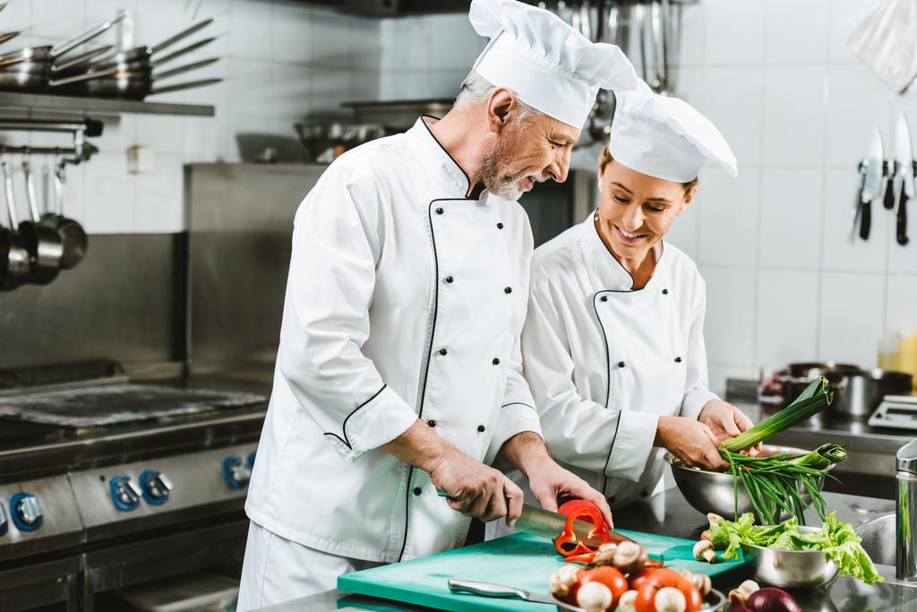 усміхнені жіночі та чоловічі кухарі в уніформі та капелюхах готують на кухні ресторану
 - Фото, зображення