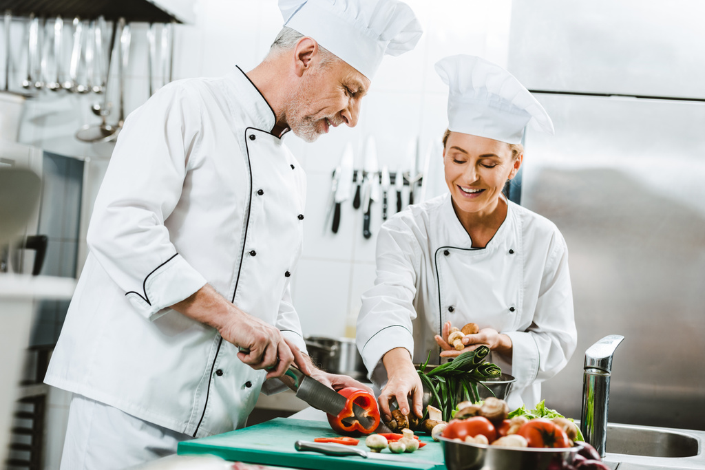 chefs femeninos y masculinos en uniforme y sombreros de cocina en la cocina del restaurante
 - Foto, Imagen