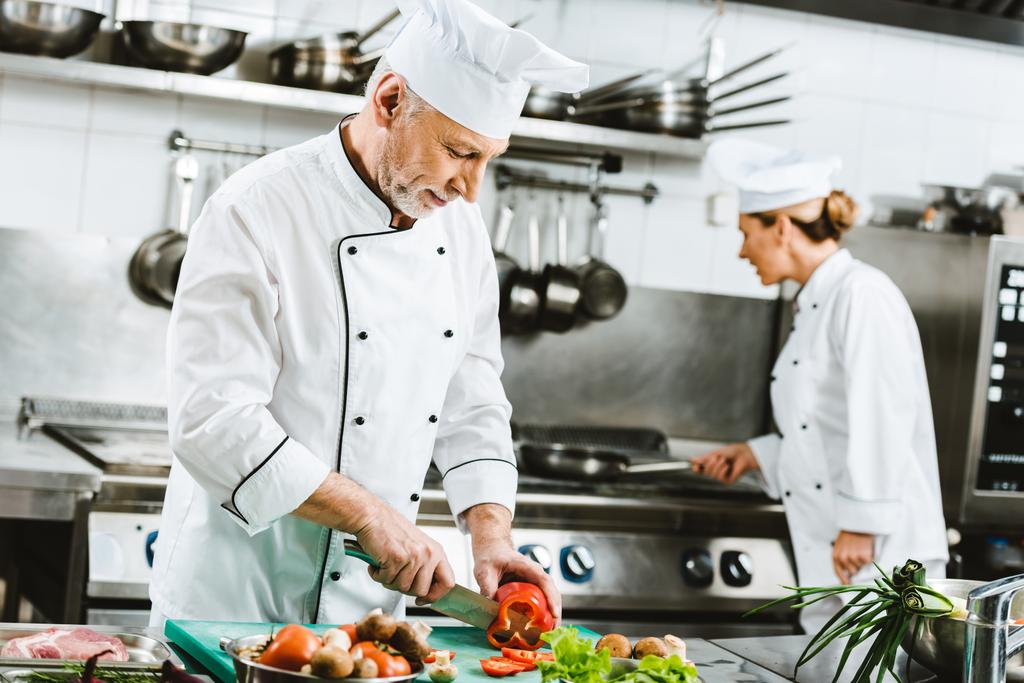 foco seletivo de chefs masculinos e femininos em uniforme preparando comida na cozinha do restaurante
 - Foto, Imagem