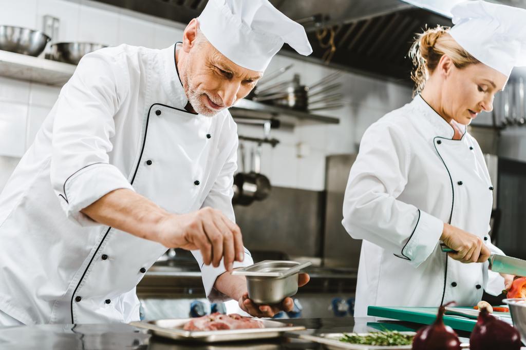 зосереджені чоловічі та жіночі кухарі в уніформі готують їжу на кухні ресторану
 - Фото, зображення