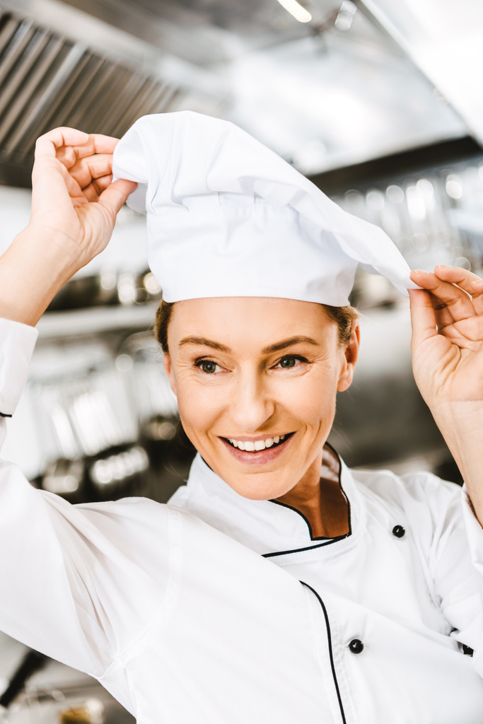 hermosa sonrisa hembra chef ajustando la tapa en la cocina del restaurante
 - Foto, imagen