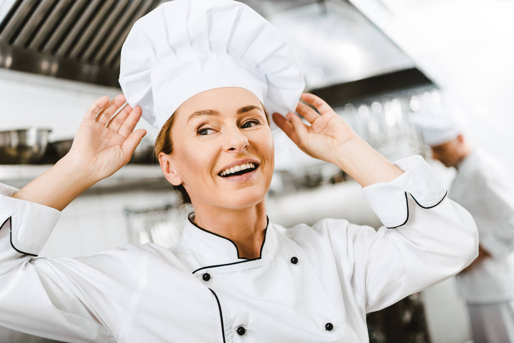 hermosa sonrisa hembra chef ajustando la tapa en la cocina del restaurante
 - Foto, Imagen