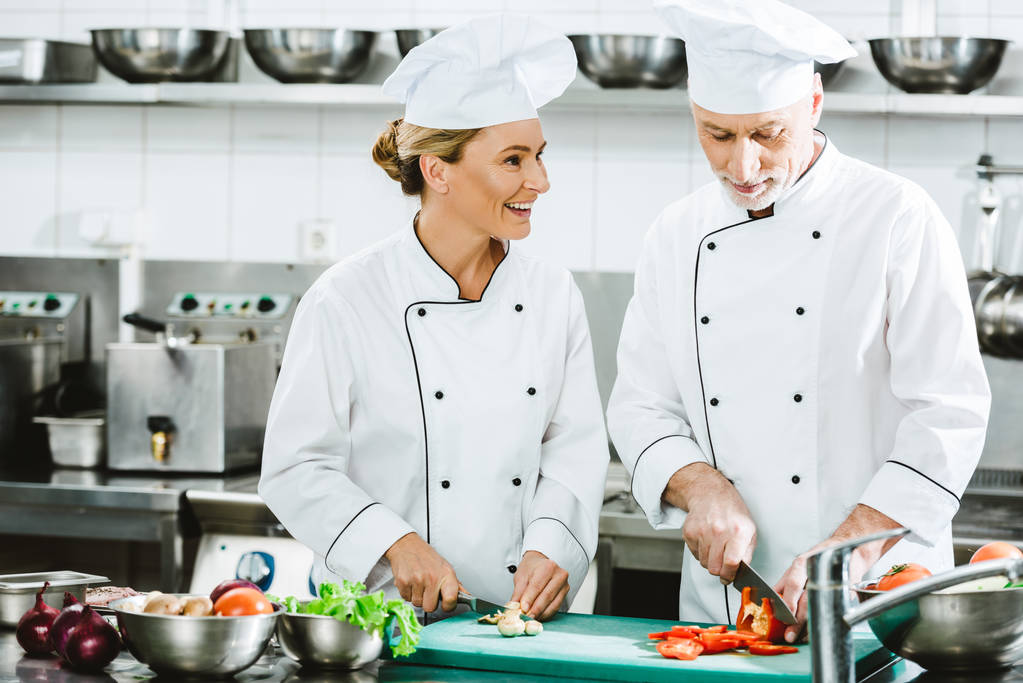 chefs femeninos y masculinos en uniforme cortando ingredientes mientras cocinan en la cocina del restaurante
 - Foto, imagen