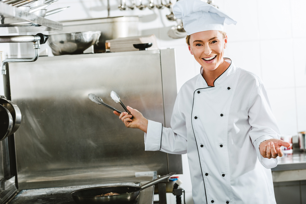 bella chef donna in uniforme con pinze da cucina mentre cucina in cucina ristorante
 - Foto, immagini
