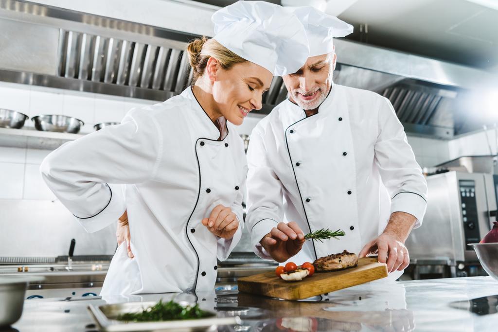 kucharze kobieta i mężczyzna w mundurze z mięsa stek na desce w kuchni restauracji - Zdjęcie, obraz
