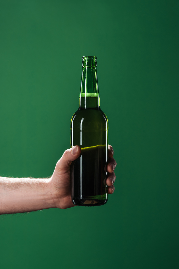 vista ritagliata di uomo che tiene bottiglia di birra isolata sul verde, concetto di giorno di San Patrizio
 - Foto, immagini
