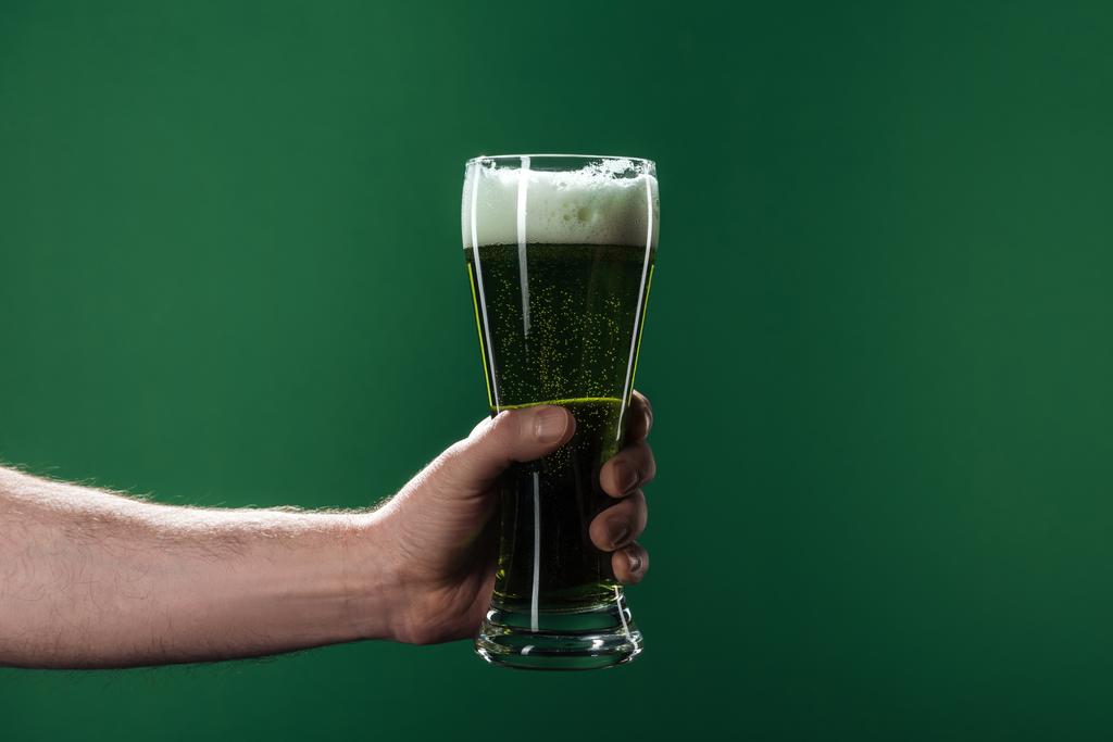 vista ritagliata di uomo che tiene i bicchieri di birra con schiuma isolata sul verde, concetto di giorno di San Patrizio
 - Foto, immagini