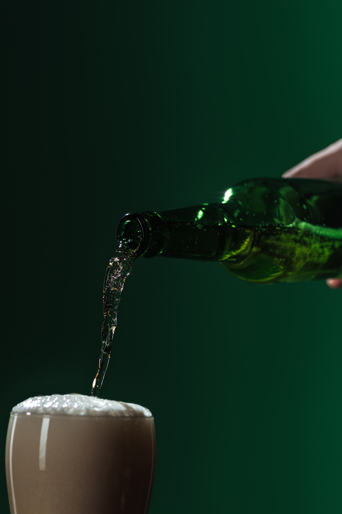 наливая пиво в стакан с пеной, изолированной на зеленой концепции дня Святого Патрика
 - Фото, изображение