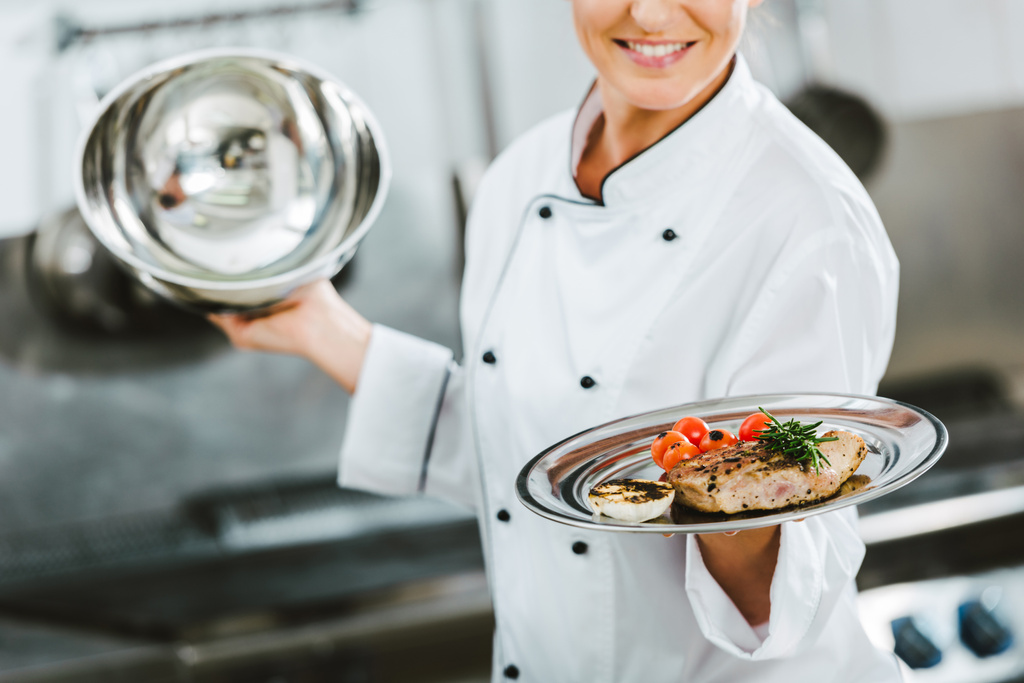 abgeschnittene Ansicht einer Köchin in Uniform, die ein Tablett mit Fleischplatte in der Restaurantküche hält - Foto, Bild