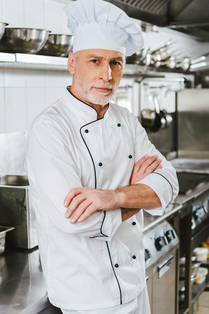komea mies kokki univormussa kädet ristissä katsoen kameraa ravintolan keittiössä
 - Valokuva, kuva