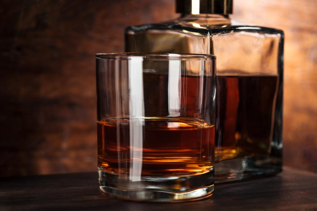 Nahaufnahme von Glas Whiskey und Flasche auf Holztisch  - Foto, Bild