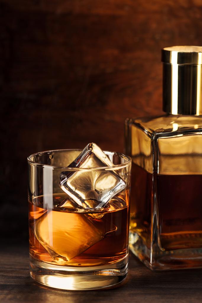 Close-up weergave van glas whisky met ijsblokjes en fles in houten tafel  - Foto, afbeelding