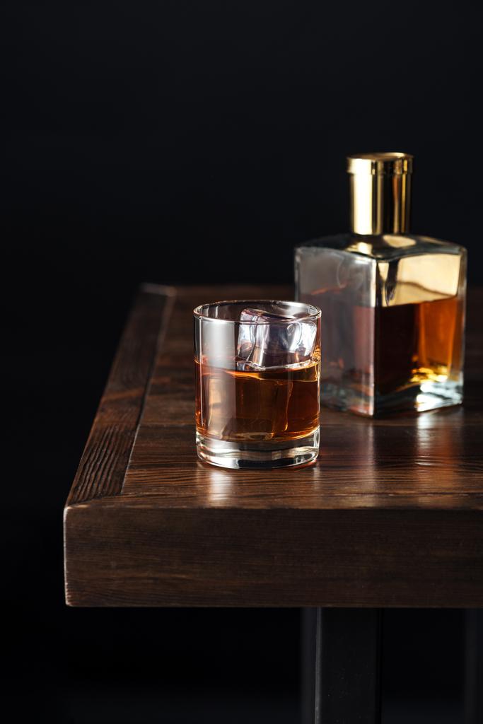 крупним планом склянка і пляшка віскі на темному дерев'яному столі ізольовані на чорному
   - Фото, зображення