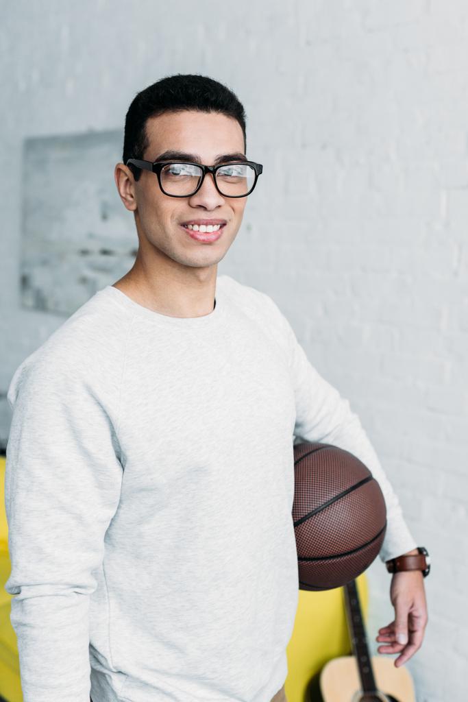fiatal kevert férfi fehér pulóver és a szemüveget tartó labdát és látszó-on fényképezőgép - Fotó, kép