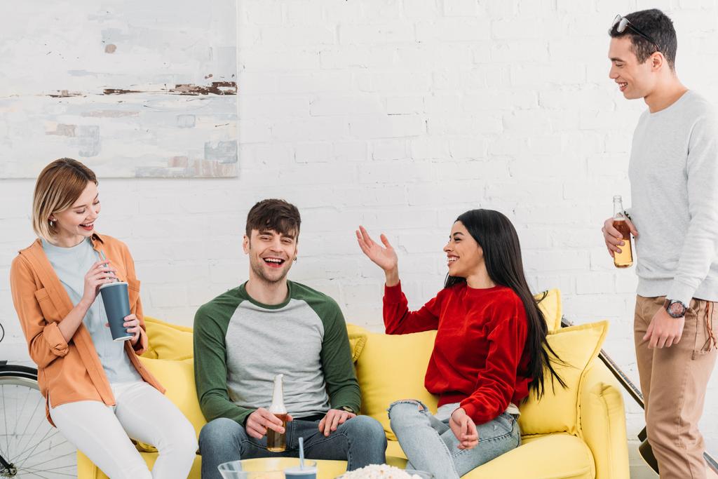 amigos multiétnicos riendo charlando mientras están sentados en la mesa amarilla en la sala de estar
 - Foto, imagen