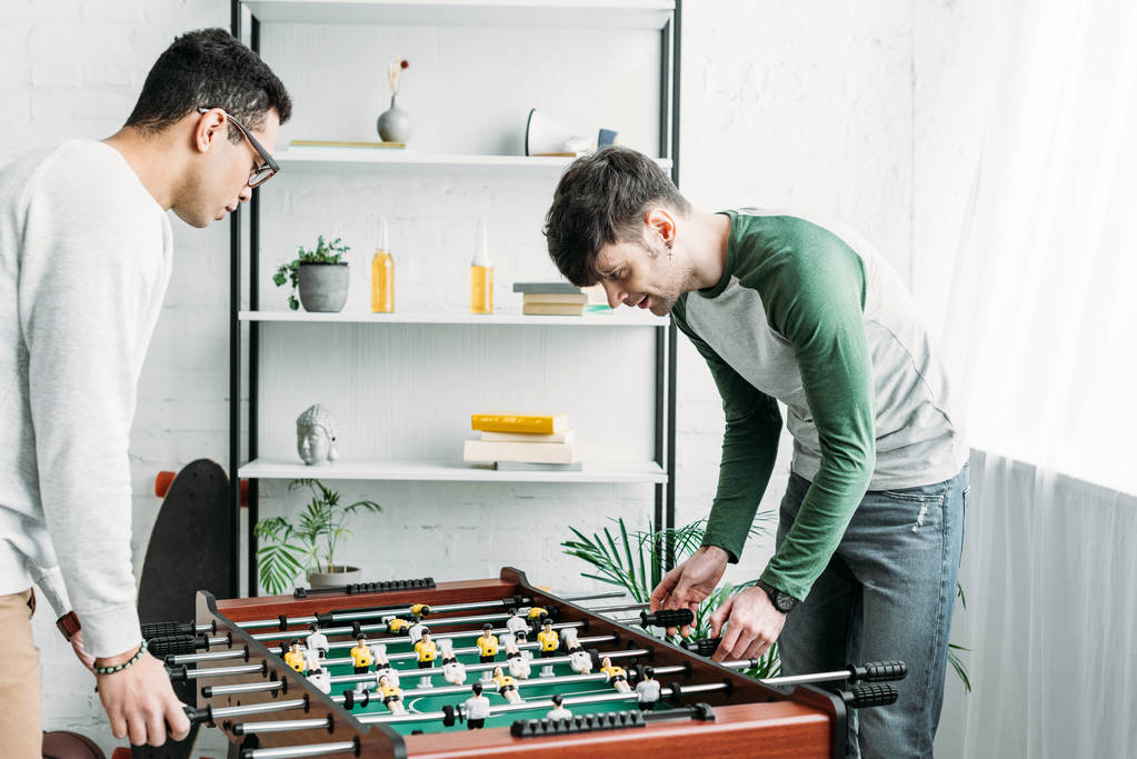 handsome multicultural friends playing table football in living room - Photo, Image