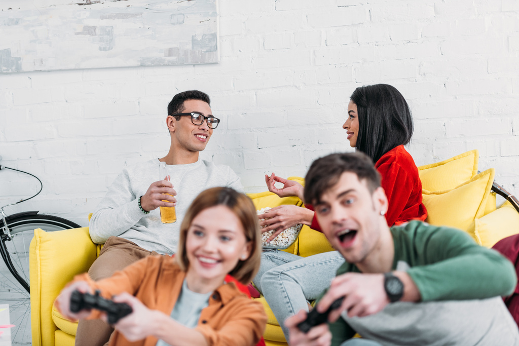 allegri amici multiculturali che si divertono a casa, giocano ai videogiochi e si godono drink e snack
  - Foto, immagini