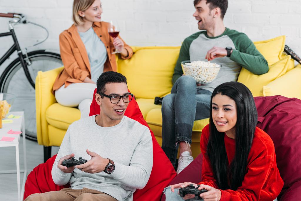 iloinen monikulttuurinen ystävät pelaavat videopeli ja nauttia juomia ja välipaloja
  - Valokuva, kuva